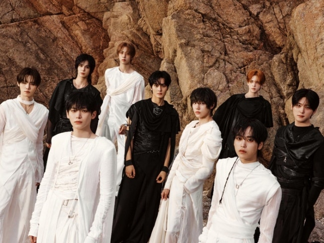 Nine CRAVITY members in black and white outfits against a rocky backdrop